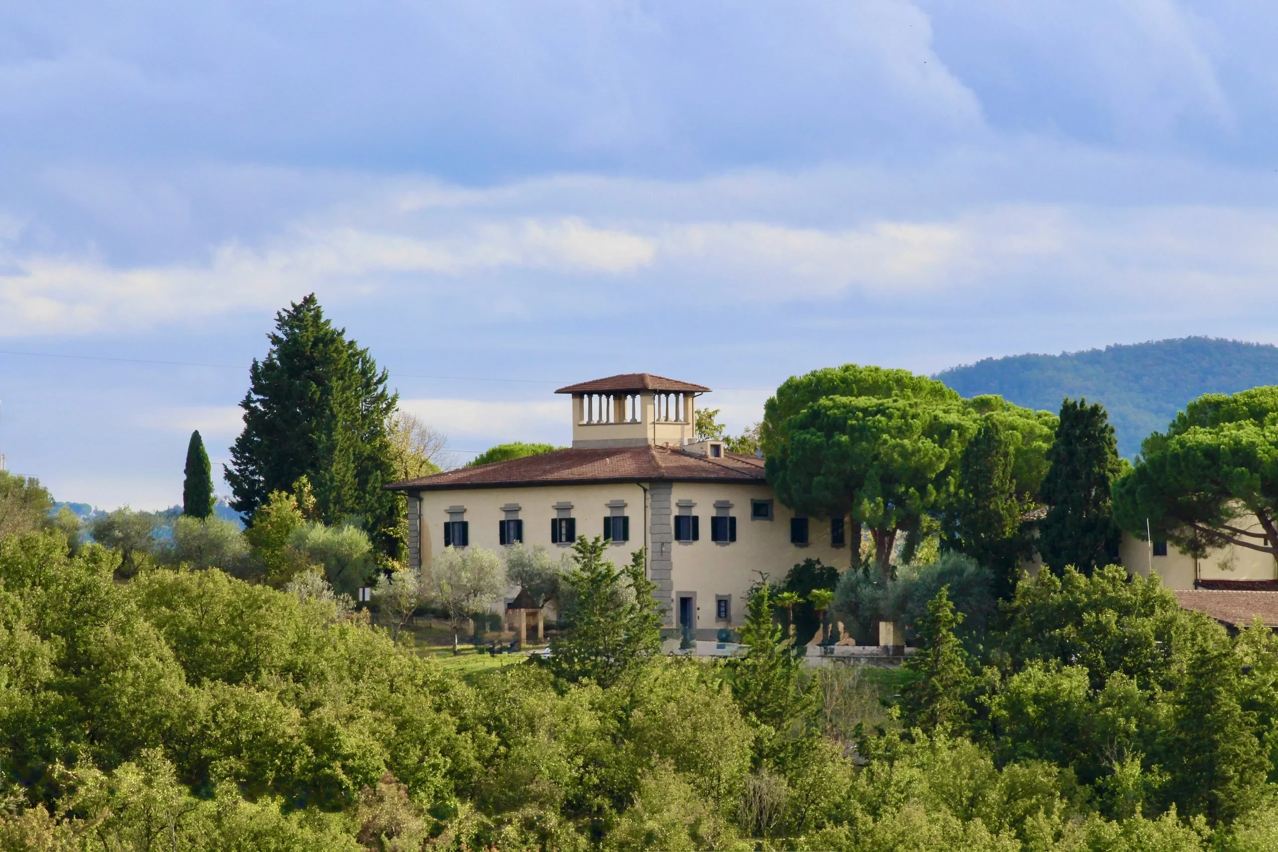 Villa italiana circondata da alberi e colline verdi.
