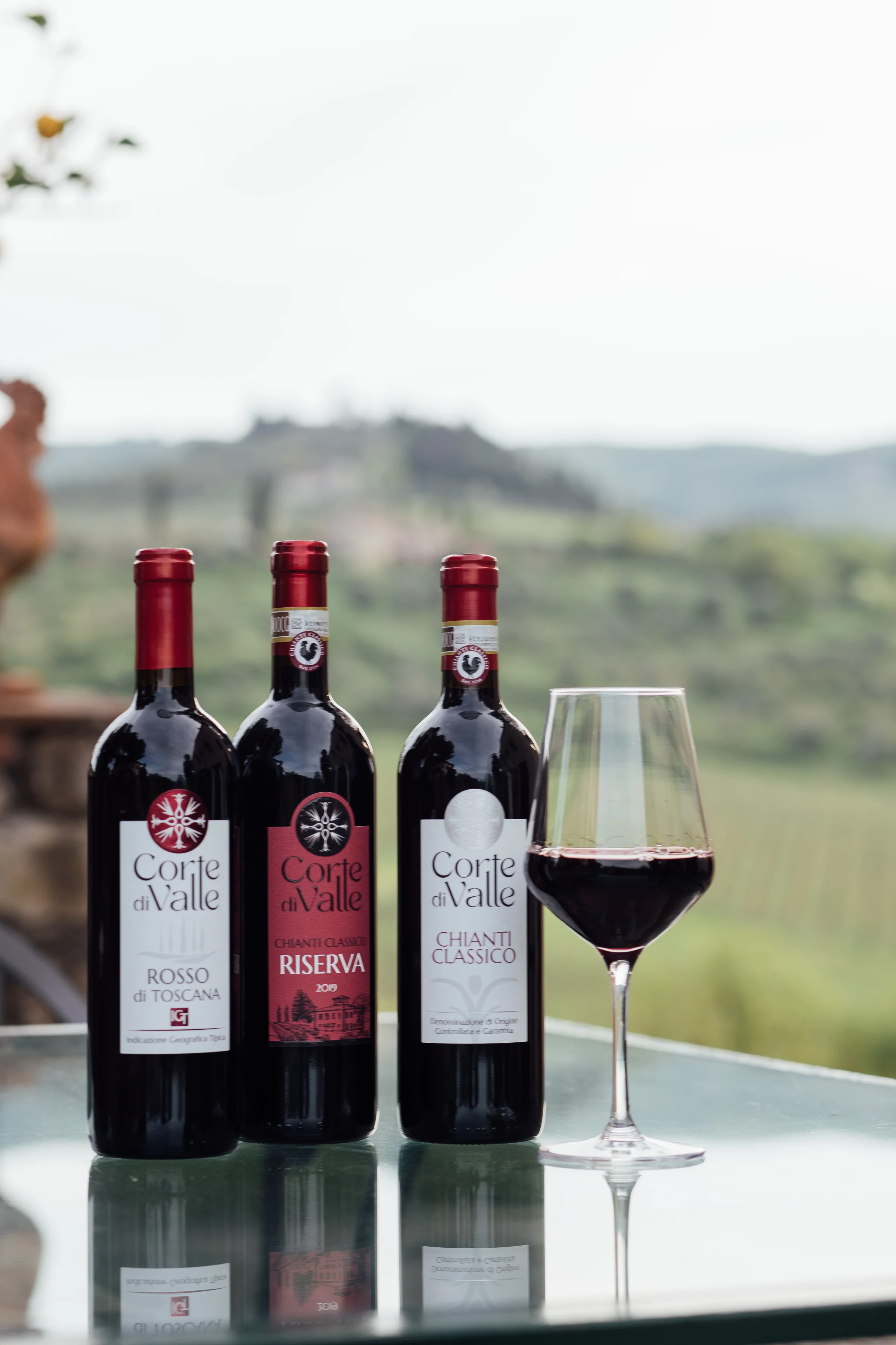 Tre bottiglie di vino con calice su tavolo.